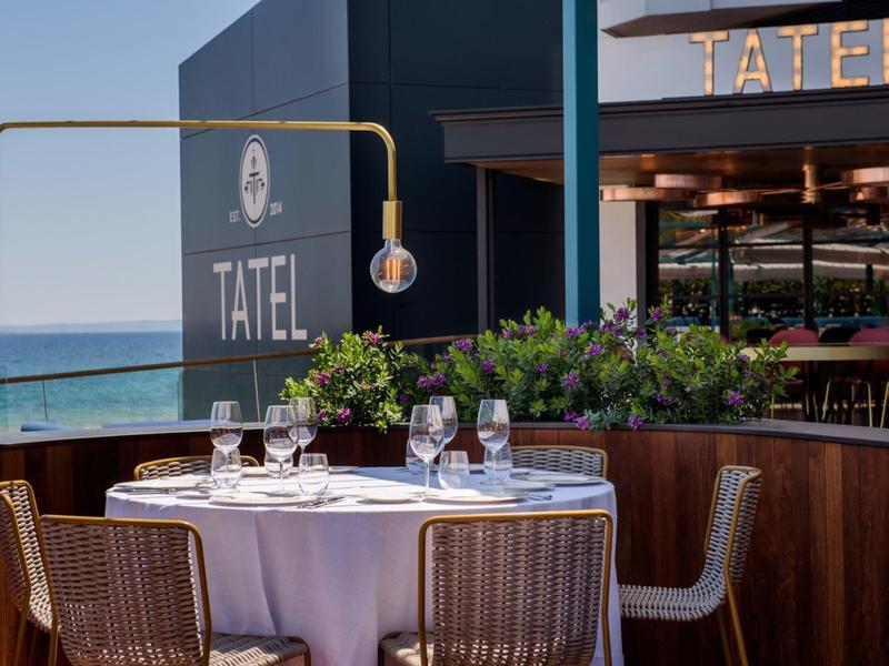 Elegant table with white tablecloths and glasses on a terrace overlooking the sea and restaurant.
