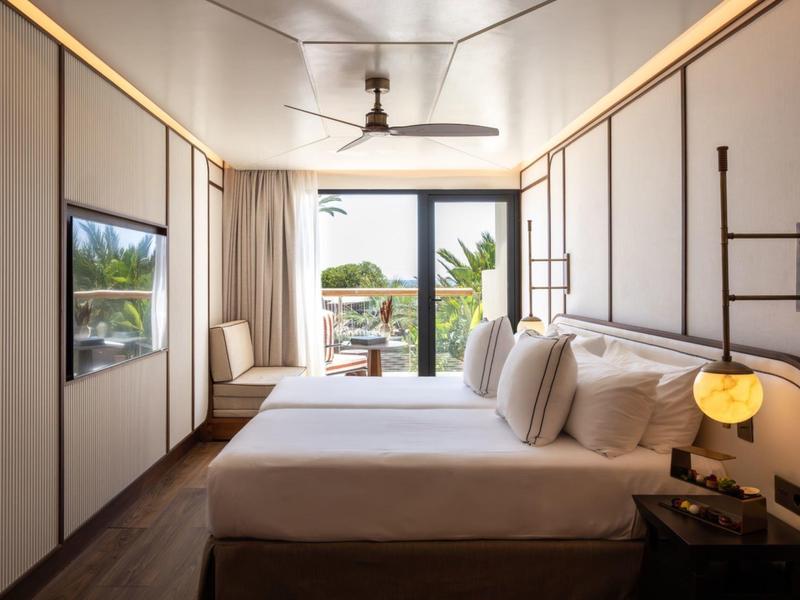 Modern hotel room with large bed, balcony, and tropical view.