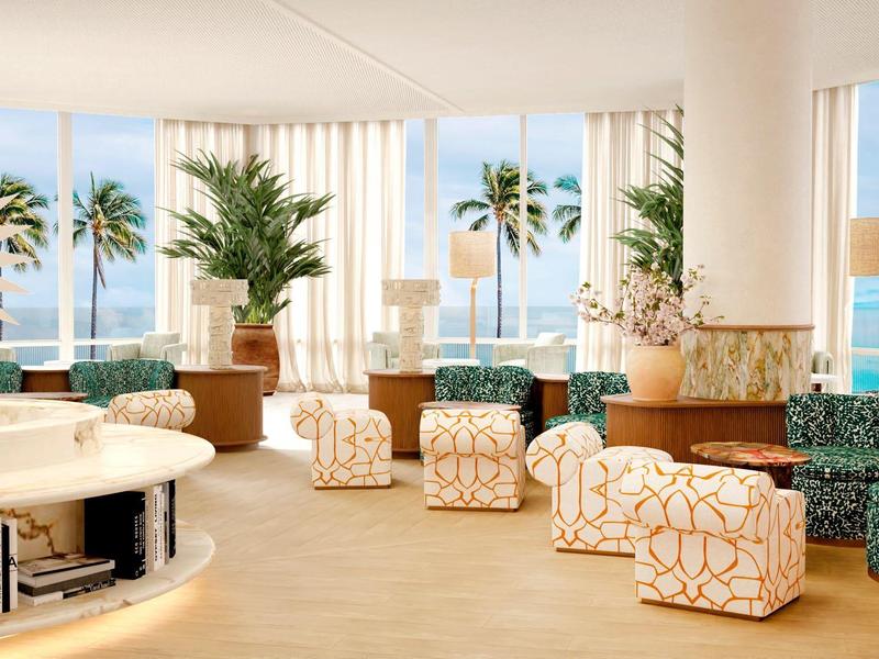 Bright modern hotel lounge with armchairs, plants, and sea view through large windows.