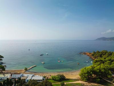 Linea costiera con spiaggia sabbiosa, acqua limpida e barche sotto un cielo azzurro.
