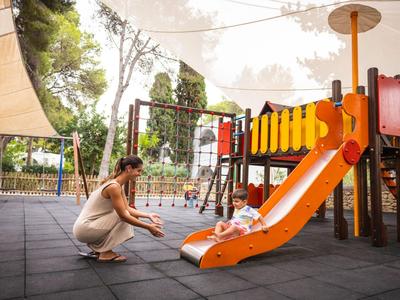Una donna aiuta un bambino a scivolare giù da uno scivolo arancione in un parco giochi.
