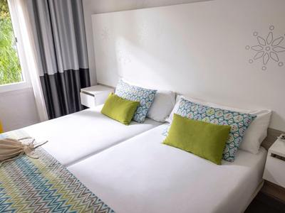 Zwei weiße Einzelbetten mit bunten Kissen und Decken in einem hellen, modernen Schlafzimmer.