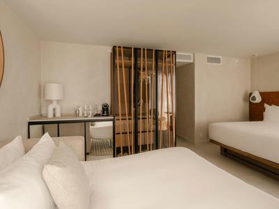 Habitación de hotel moderna con dos camas, un gran espejo y una mesa pequeña con botellas de agua.