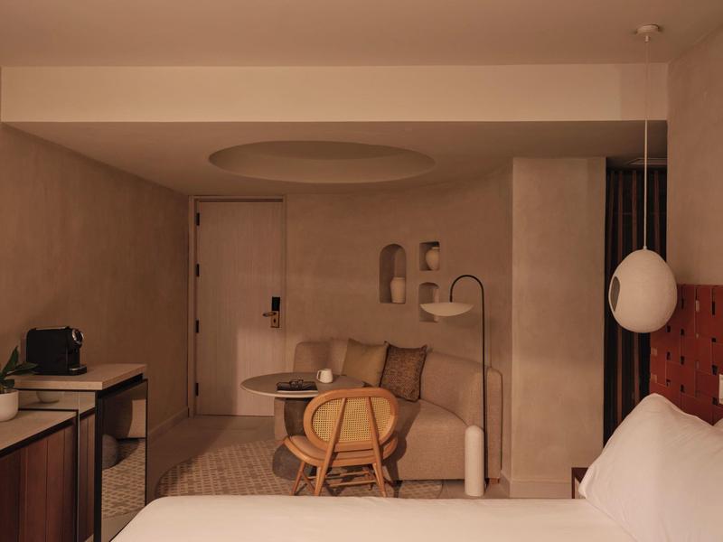 Acogedora habitación de hotel con área de estar moderna, escritorio y cama confortable en tonos cálidos.