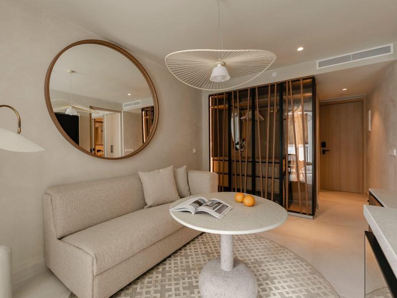 Habitación de hotel decorada con estilo moderno con sofá, espejo redondo y mesa pequeña redonda.