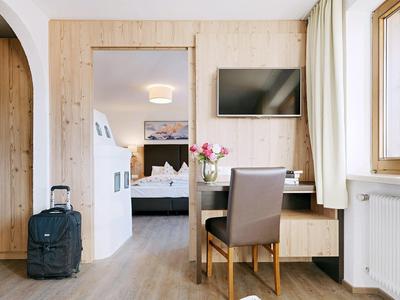 Lichte hotelkamer met bureau, stoel, tv en open deur naar slaapkamer.