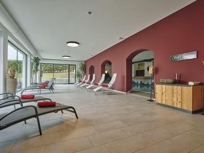 Moderner Wellnessbereich mit Liegestühlen, roten Wänden und großen Fenstern mit Blick auf den Garten.