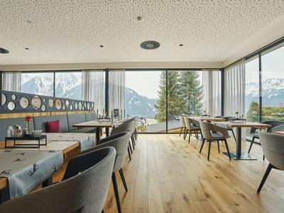 Moderner Gastraum mit Holzboden, großen Panoramafenstern und Bergsicht, bequeme Stühle und Tische.
