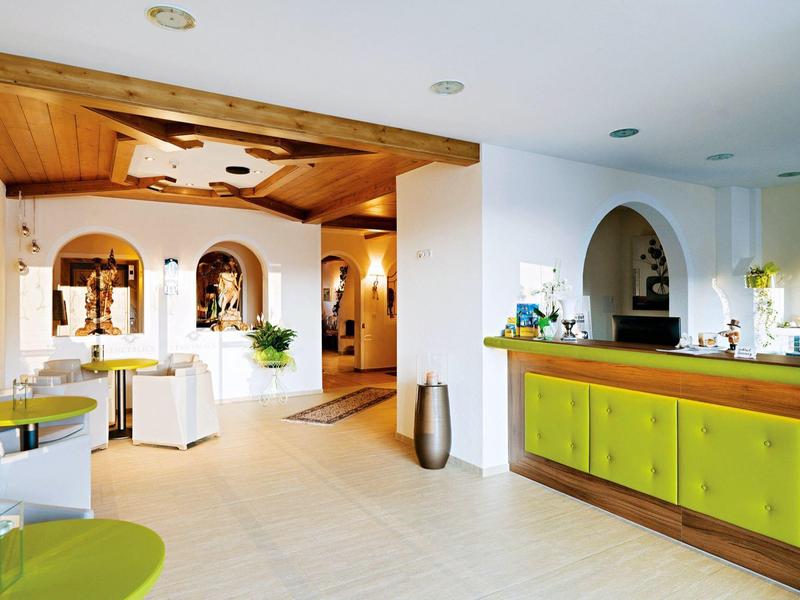 Licht restaurant met groene stoelen, houten balken aan het plafond en witte muren.