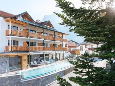 Modernes Hotel mit Holzverkleidung, großen Balkonen und langem Außenpool bei Tageslicht.