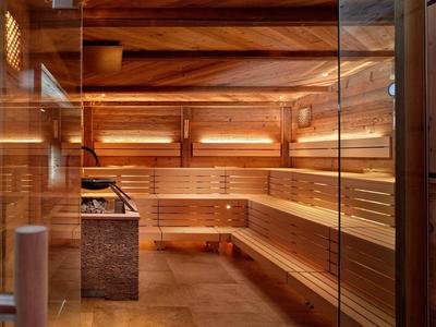 Modern wooden sauna room with warm lighting and clear glass partition.
