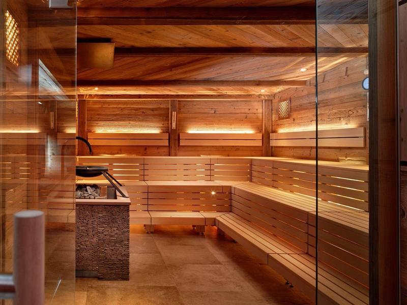Modern wooden sauna room with warm lighting and clear glass partition.