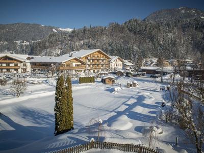 Paisaje cubierto de nieve con un gran hotel frente a montañas boscosas bajo un cielo azul despejado.