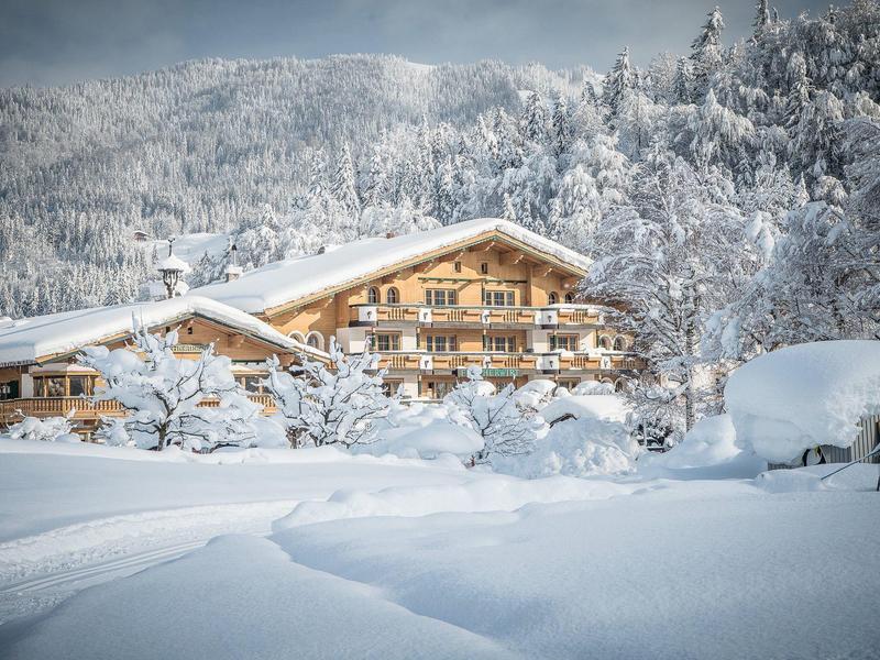 Chalet de madera en un paisaje invernal nevado con árboles y montañas cubiertos de nieve al fondo