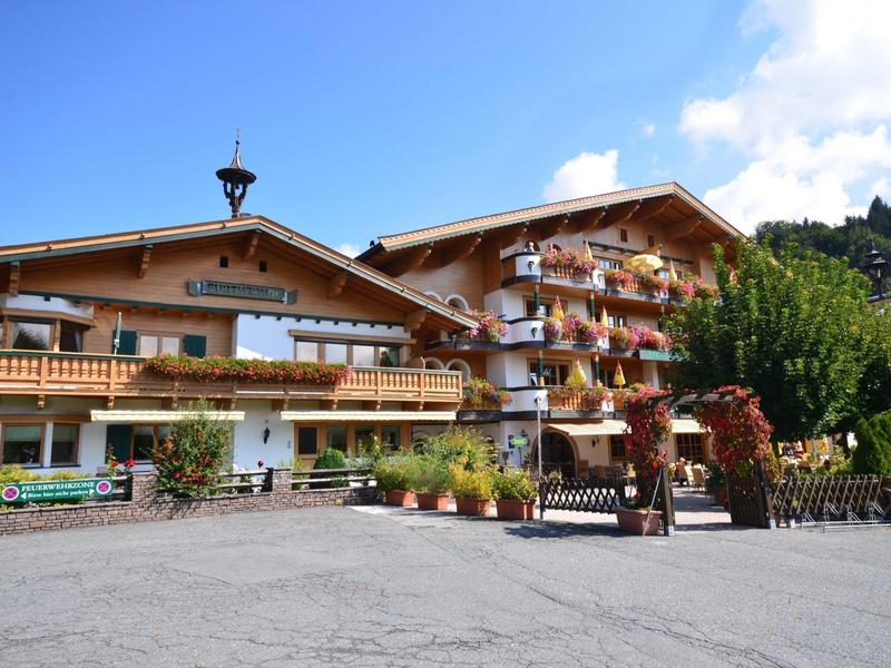 Hotel chalet tradicional con balcones y decoración floral en paisaje alpino.