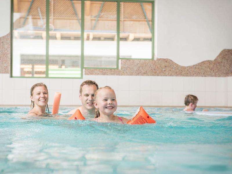 Tres niños con manguitos juegan en la piscina cubierta, dos más al fondo.