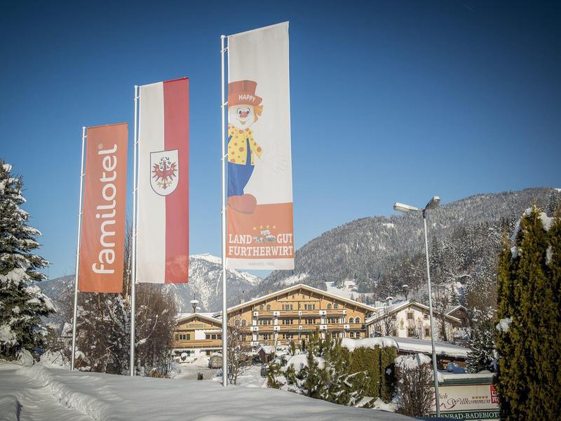 Tres banderas frente a un hotel cubierto de nieve con montañas al fondo bajo un cielo despejado.