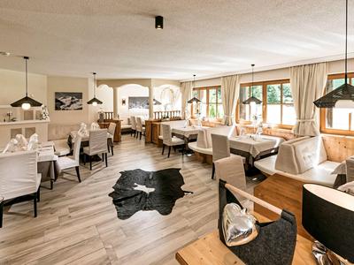 Helles Restaurant mit Holzboden, weißen Stühlen und großen Fenstern mit Blick ins Freie