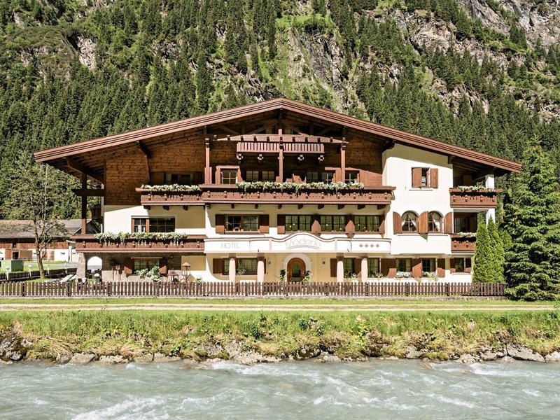 Gran chalet con detalles de madera junto a un río de montaña en un paisaje alpino.