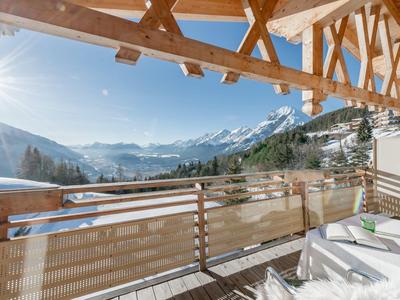 Balkon mit Liegestühlen und Holzgeländer mit Blick auf schneebedeckte Berge bei sonnigem Himmel.