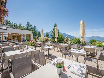 Terrazza d'hotel eccezionale con vista sulle montagne, tavoli apparecchiati e ombrelloni sotto un cielo limpido.