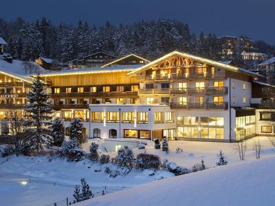 Beleuchtetes Hotel in verschneiter Winterlandschaft mit Wald im Hintergrund.