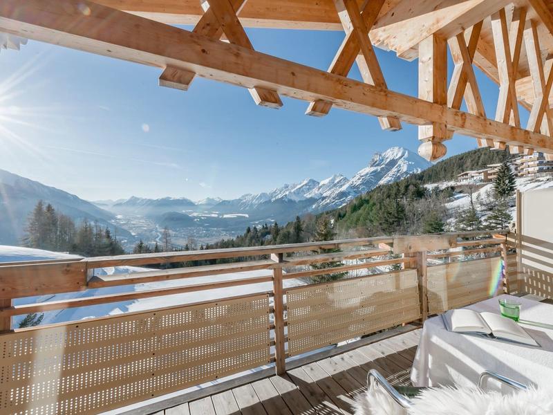 Balkon mit Liegestühlen und Holzgeländer mit Blick auf schneebedeckte Berge bei sonnigem Himmel.