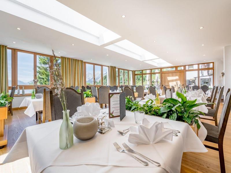 Heller, moderner Speisesaal mit großen Fenstern, gedeckten Tischen und grünen Pflanzen.