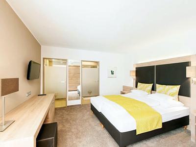 Nowoczesny pokój hotelowy z podwójnym łóżkiem, żółtą narzutą i telewizorem LCD.