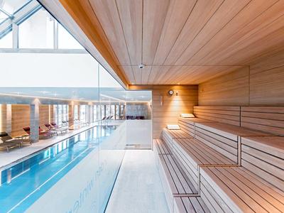 Nowoczesna strefa wellness z basenem i drewnianą sauną w jasnym, przestronnym pomieszczeniu.