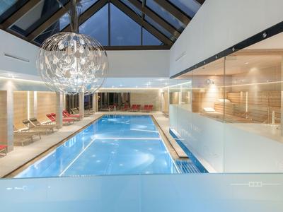 Innenbereich eines Hotels mit beheiztem Pool, modernen Liegestühlen und großen Glasfenstern.