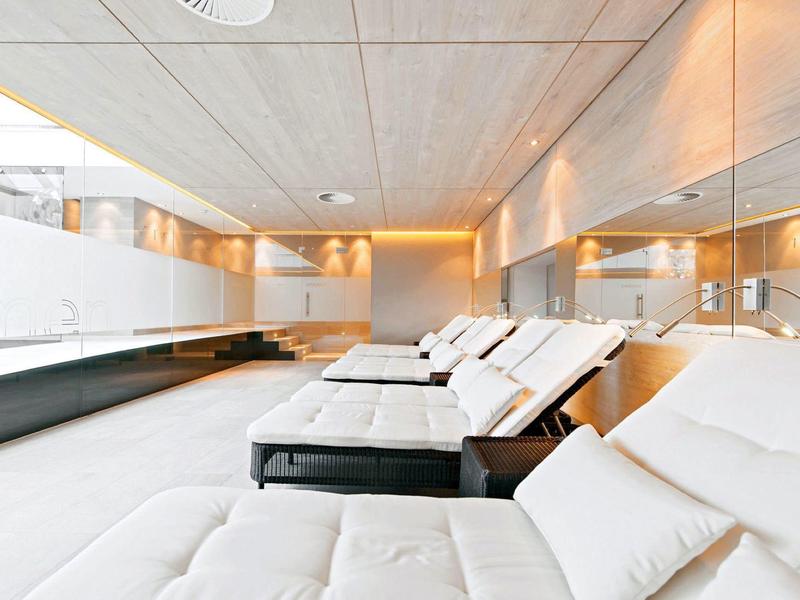 Nowoczesne, jasne leżanki wellness z białymi poduszkami i lustrzaną ścianą w hotelu.