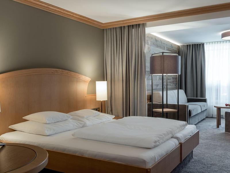 Przytulny pokój hotelowy z podwójnym łóżkiem, sofą i naturalnym światłem z dużego okna.