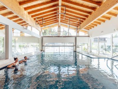 Indoor pool with wooden ceiling and two people in water at a hotel.