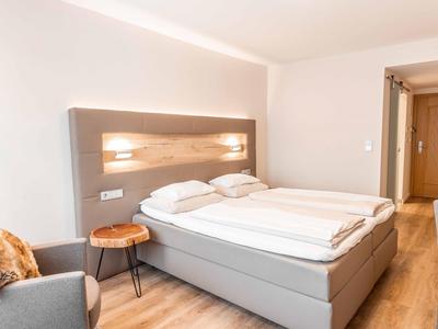 Bright hotel room with large double bed, wooden floor, and seating area with gray armchair.