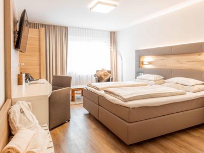Modern hotel room with double bed, wooden flooring, and cozy seating area by the window.