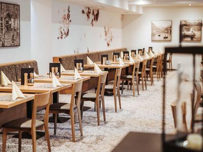 Eleganter Speiseraum mit langen Holztischen, dekorierten Stühlen und warmem Licht.