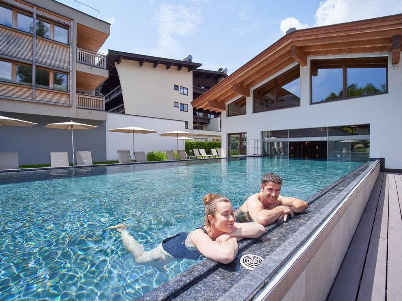 Two people relax in an outdoor pool of a modern hotel with glass railing.