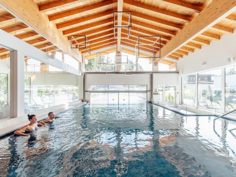 Indoor pool with wooden ceiling and two people in water at a hotel.