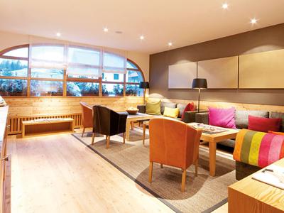 Gemütlicher Hotel-Loungebereich mit bunten Sesseln, einem Sofa und großen Fenstern.