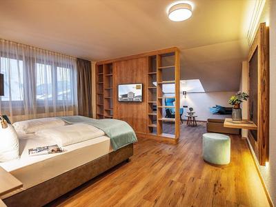 Gezellige hotelkamer met houten vloer, bed, bureau en glazen houten scheidingswand.