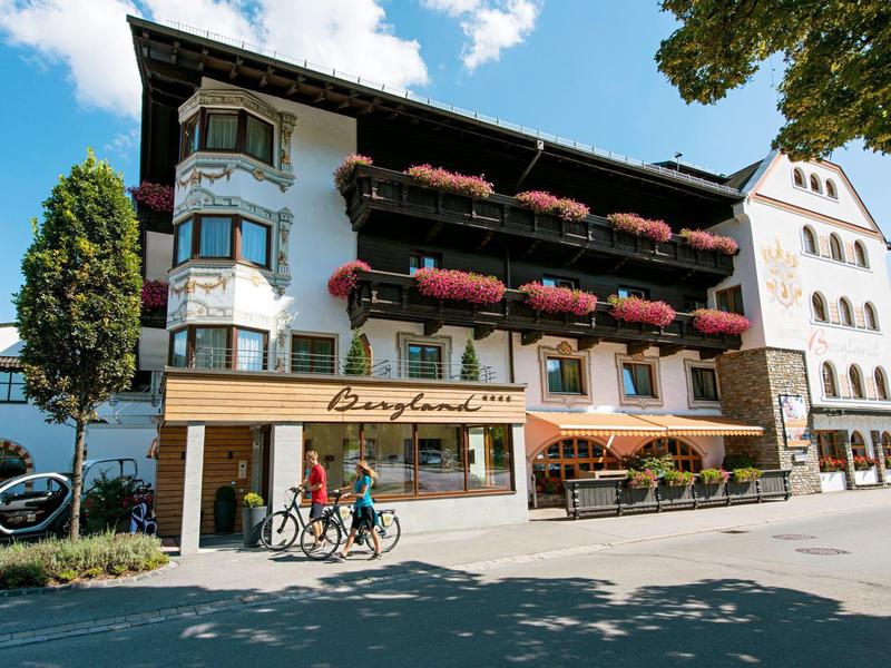 Hotel met balkons, bloembakken en terras onder een zonnige hemel met fietsers ervoor.