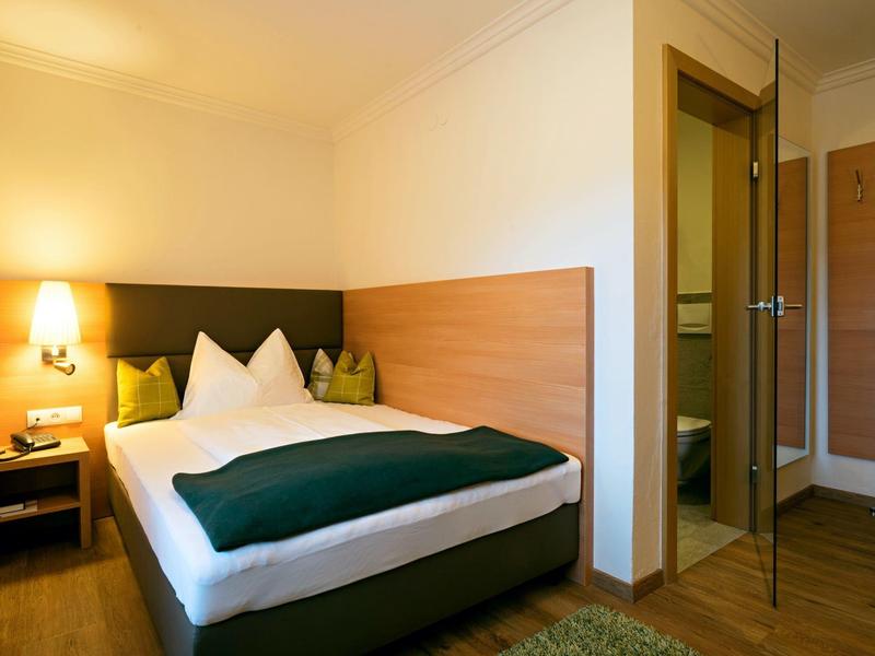 Gezellige hotelkamer met tweepersoonsbed, groene bedloper en warm licht.