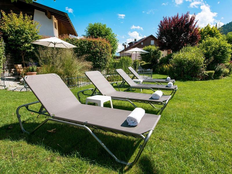 Ligstoelen met witte handdoeken op groen gazon voor huizen en bomen bij zonnig weer.