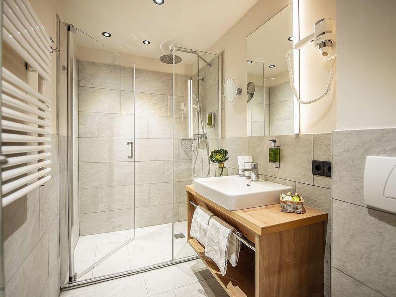 Moderne badkamer met glazen douche, houten wastafel en grote spiegels in neutrale tinten.