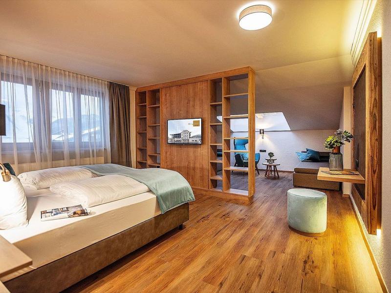 Gezellige hotelkamer met houten vloer, bed, bureau en glazen houten scheidingswand.