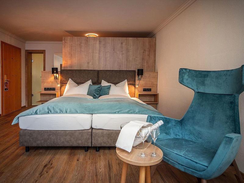Modern ingerichte hotelkamer met groot bed, houten vloer en blauwe stoel.