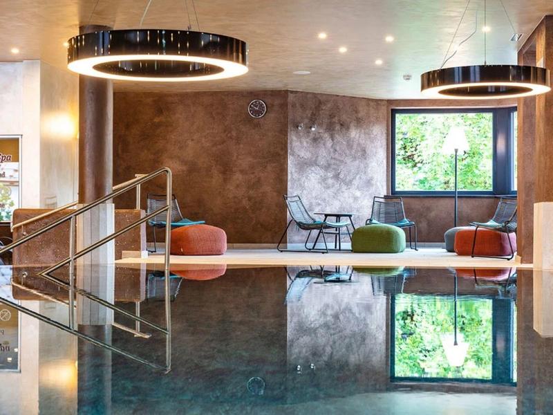 Moderne hotellobby met binnenzwembad, kleurrijke zitplaatsen en grote ramen met natuurlijk licht.