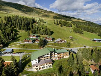 Grüne Alpenlandschaft mit verstreuten Häusern, Wiesen und bewaldeten Hügeln unter blauem Himmel.