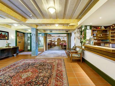 Helle Hotellobby mit Rezeption, Teppichen, Sitzbereich und Blick in angrenzenden Raum